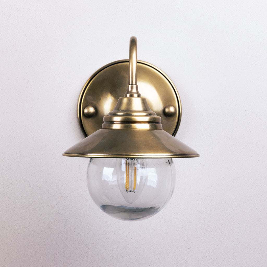 Brass wall-mounted light fixture with clear glass shade on a white background