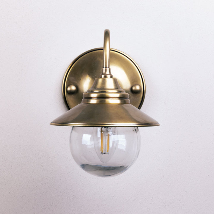 Brass wall-mounted light fixture with clear glass shade on a white background
