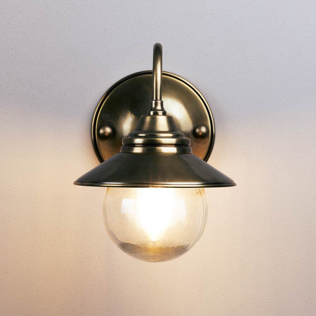 Brass wall-mounted light fixture with glass shade on a neutral background