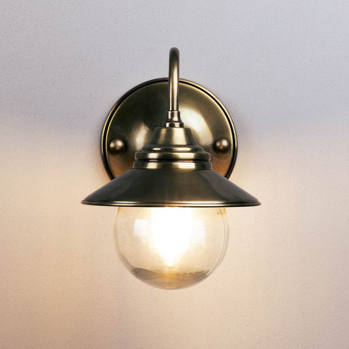 Brass wall-mounted light fixture with glass shade on a neutral background