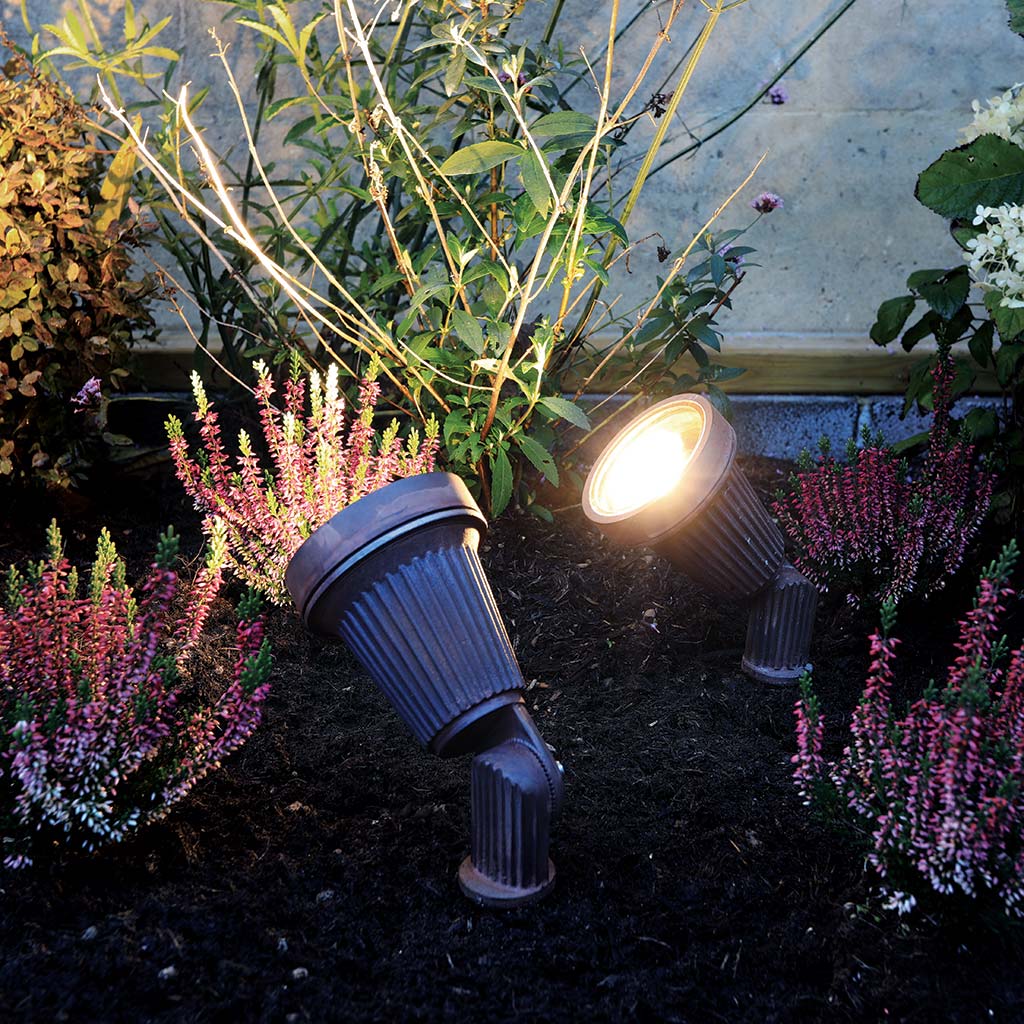 Two outdoor garden lights illuminating a garden with plants and flowers.