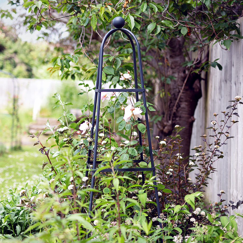 Black metal garden trellis with climbing plants in a garden setting