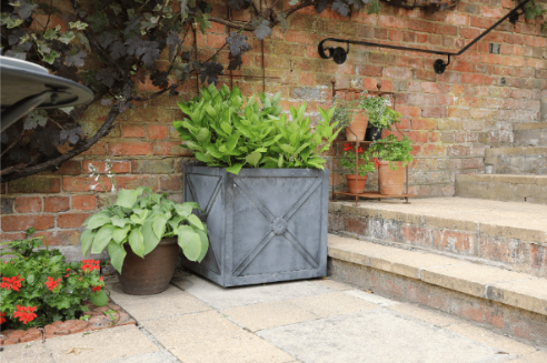 Potted plants in front of a brick wall with a garden bench.