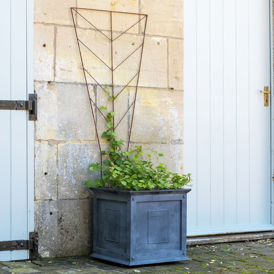 Decorative Deco Planter Trellis with plants in a blue planter against a stone wall.