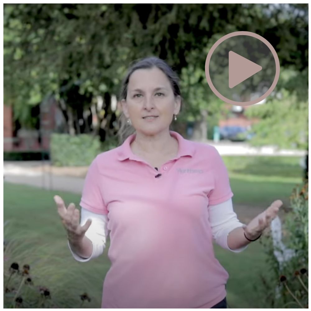 Woman in pink shirt standing outdoors with a play button overlay