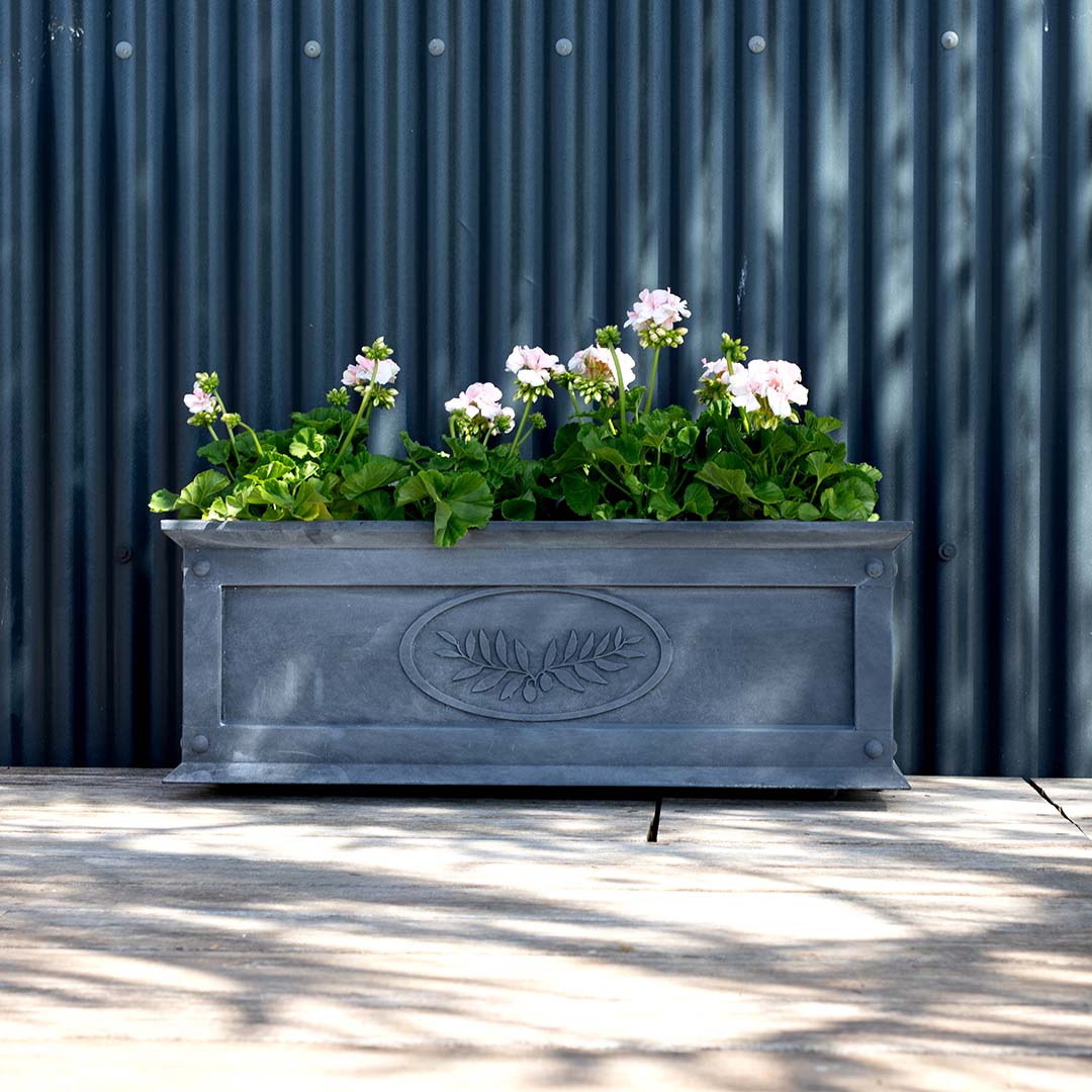 Decorative metal planter with flowers against a corrugated metal wall.
