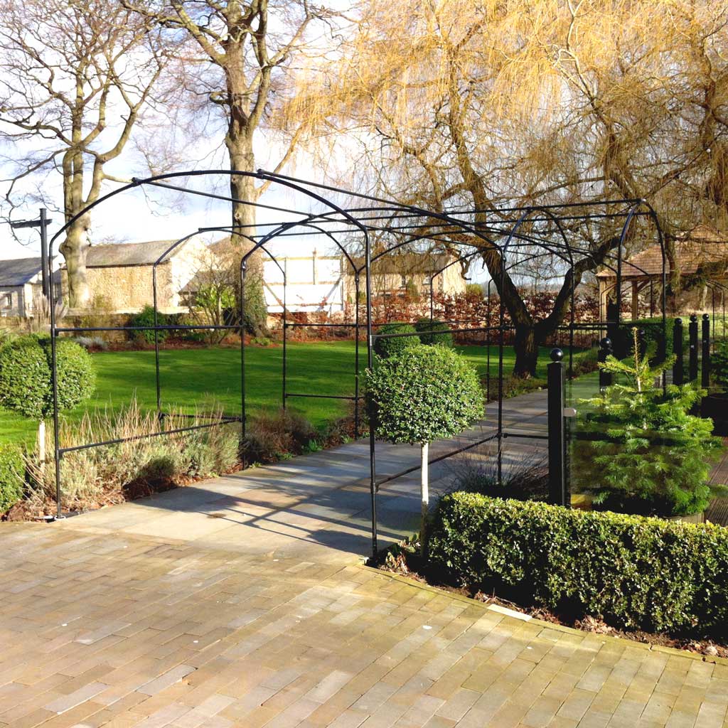 Garden pathway with metal archway, greenery, and paved walkway.
