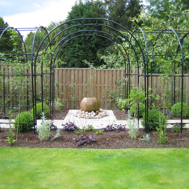 Garden with metal arches, a stone sculpture, and greenery.