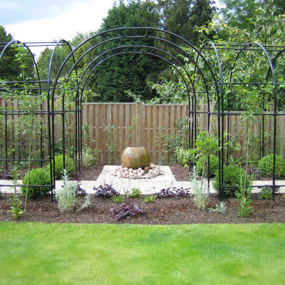Garden with metal arches, a stone sculpture, and greenery.