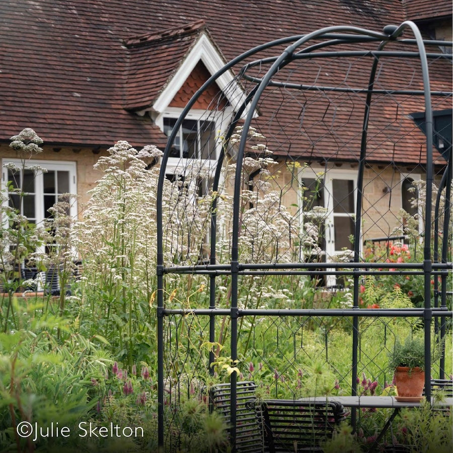 Closeup of the agriframes round arch in front of a flowerbed and cottage