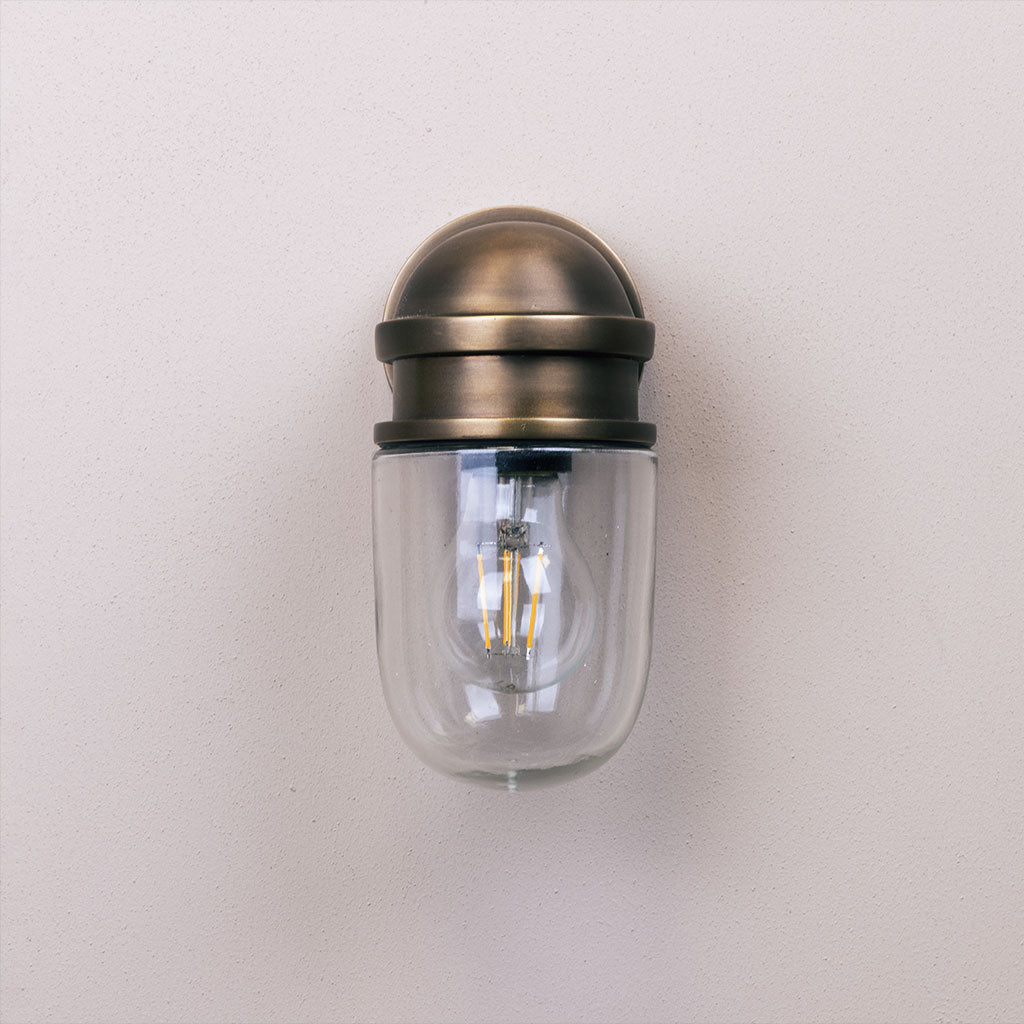 Wall-mounted light fixture with glass cover and brass finish on a plain background