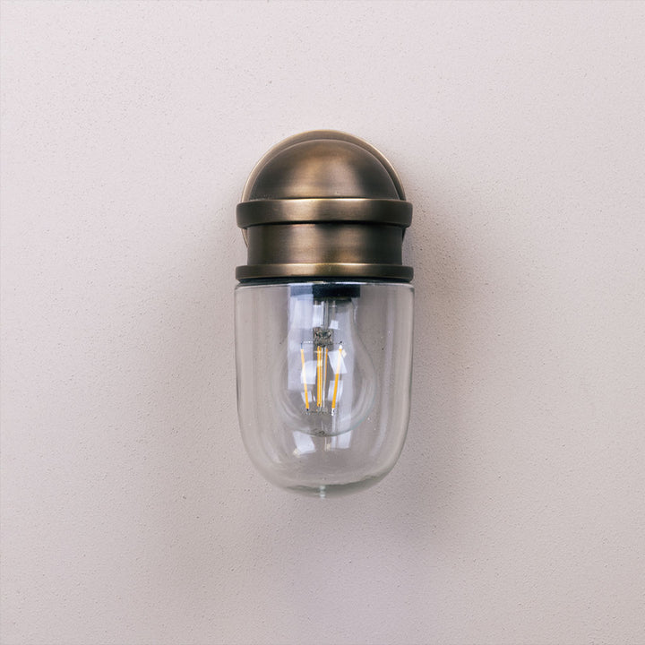 Wall-mounted light fixture with glass cover and brass finish on a plain background