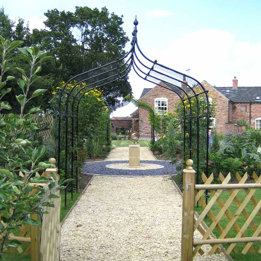 Gothic pergola over a gravel path with a view of a garden sculpture beyond