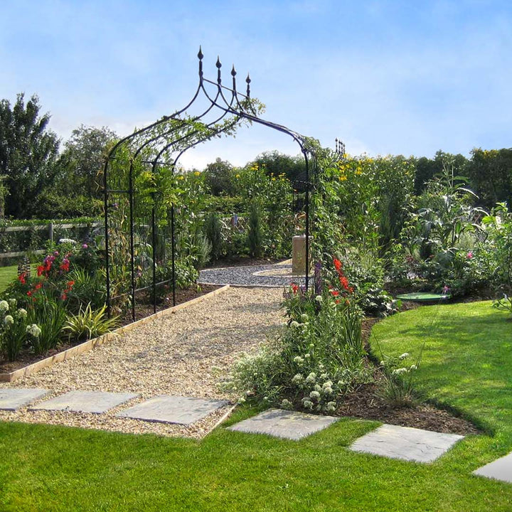 Gothic arch over gravel path, near lush lawn and flower beds