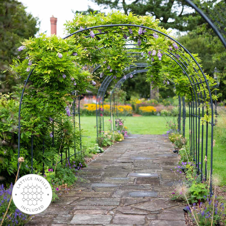 Garden archway with stone pathway leading to a garden with flowers and greenery.
