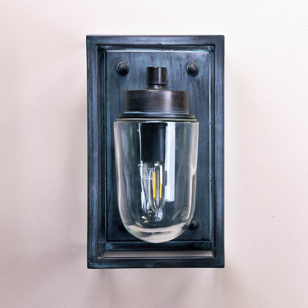 Wall-mounted light fixture with glass shade and metallic frame on a neutral background