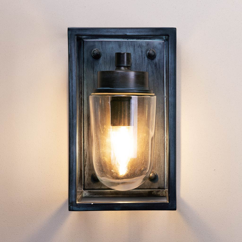 Wall-mounted light fixture with glass cover and black frame on a white wall.