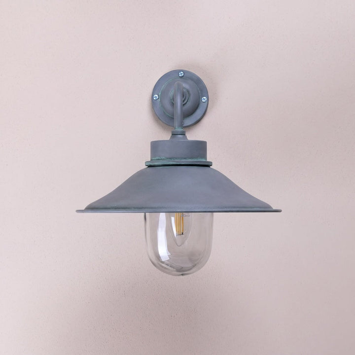 Agriframes bruton outdoor wall lamp in an old iron finish with its bulb unlit on a neutral wall. 