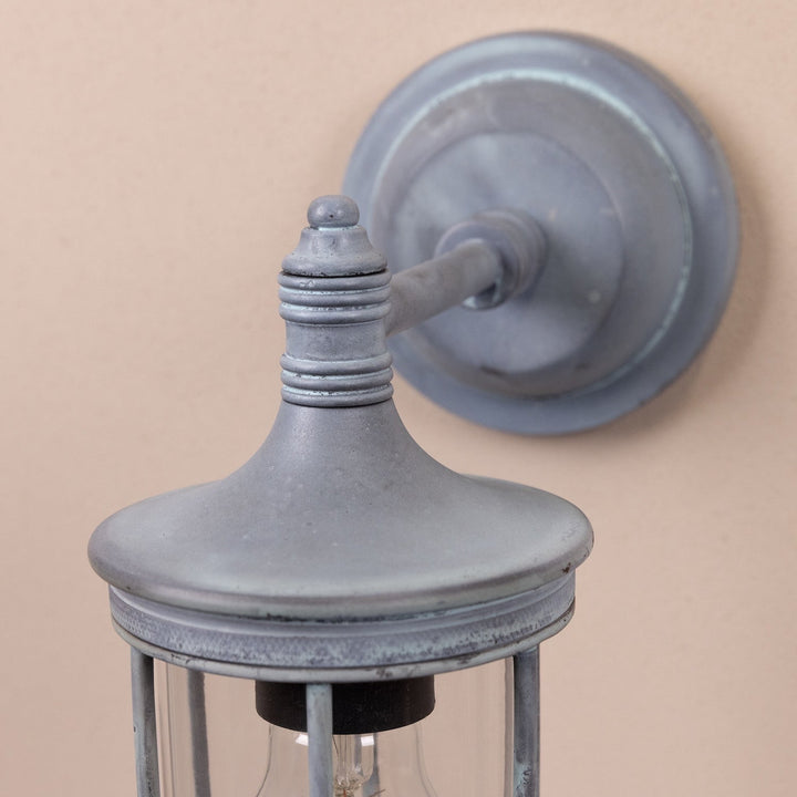 Close up of the Agriframes hampstead outdoor wall lamp in an old iron finish with its bulb unlit on a neutral wall. 
