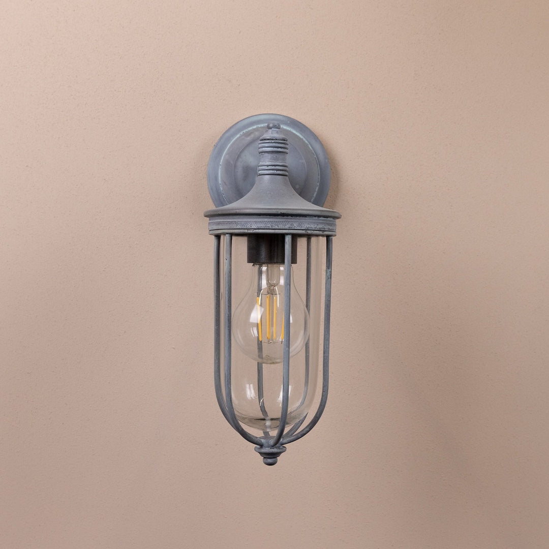 Agriframes hampstead outdoor wall lamp in an old iron finish with its bulb unlit on a neutral wall. 