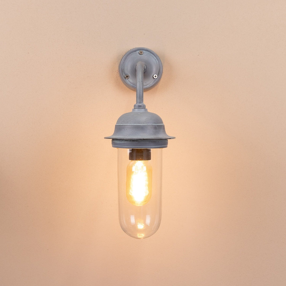 Agriframes pewsey outdoor wall lamp in an old iron finish with its bulb lit on a neutral wall. 