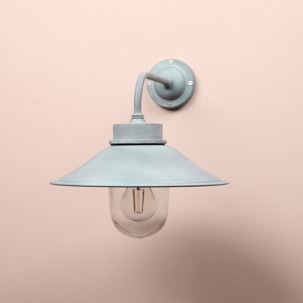 Agriframes bruton outdoor wall lamp in a verdigris finish with it's bulb unlit on a neutral-coloured wall. 