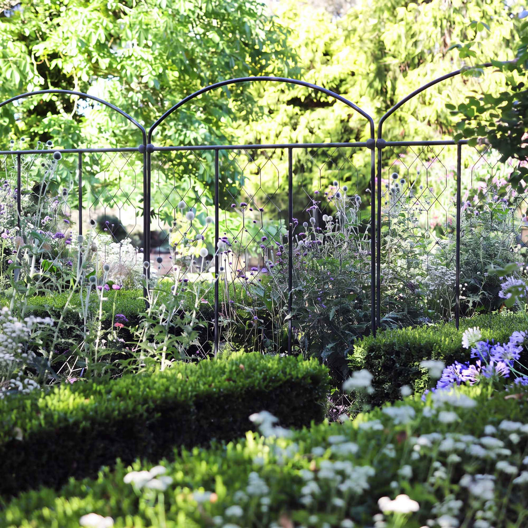 Three monet fencing screens in a row installed in a flowerbed surrounded by manicured hedges 