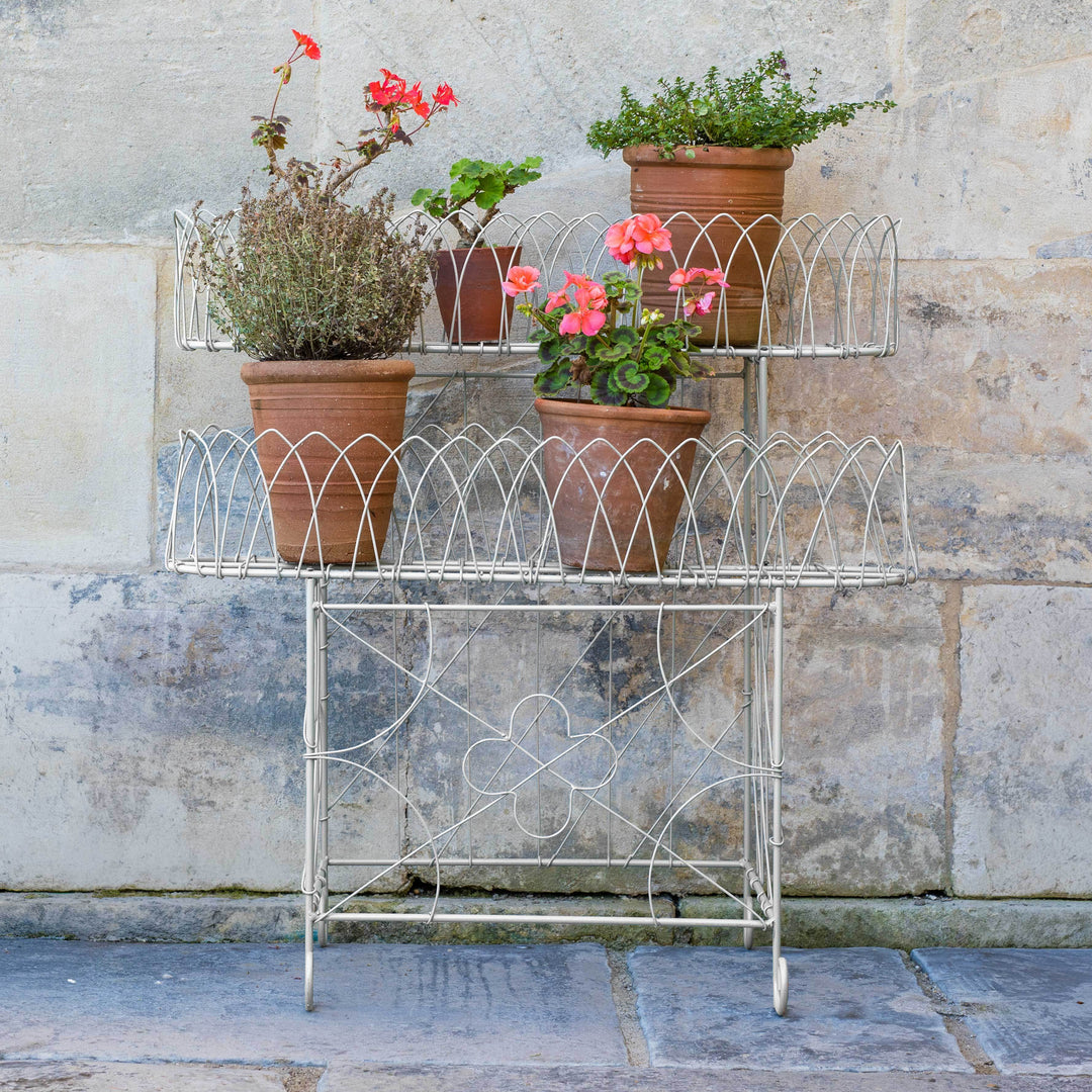 Victorian Wirework Plant Stand with potted plants against a stone wall.