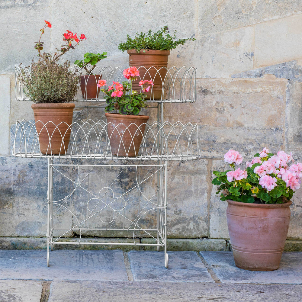 Victorian Wirework Plant Stand with potted plants against a stone wall.