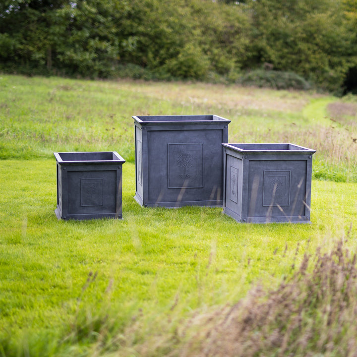Three RHS Heritage Zinc Planters on a grassy field with greenery in the background