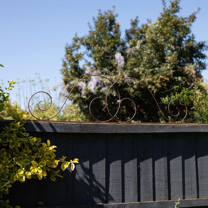Decorative metal Agriframes Elegance Fence Top Trellis on a wooden surface with trees in the background