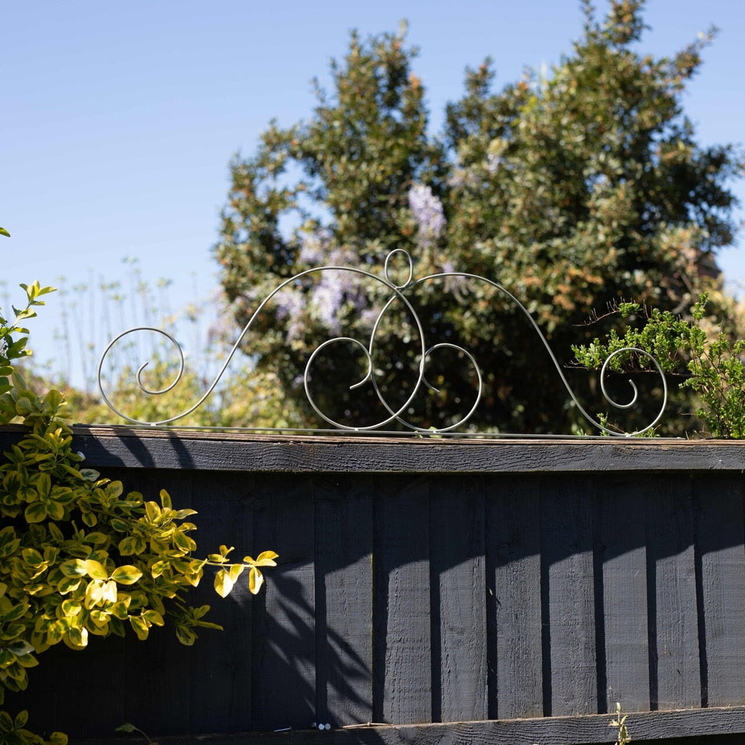 Decorative metal Agriframes Elegance Fence Top Trellis on a wooden structure with trees in the background