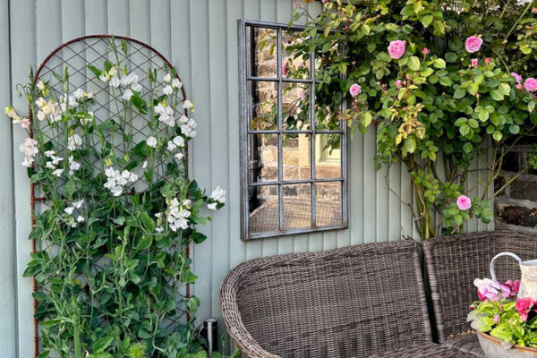 Outdoor setting with wicker furniture, flowers, and a mirror on a light blue wall.