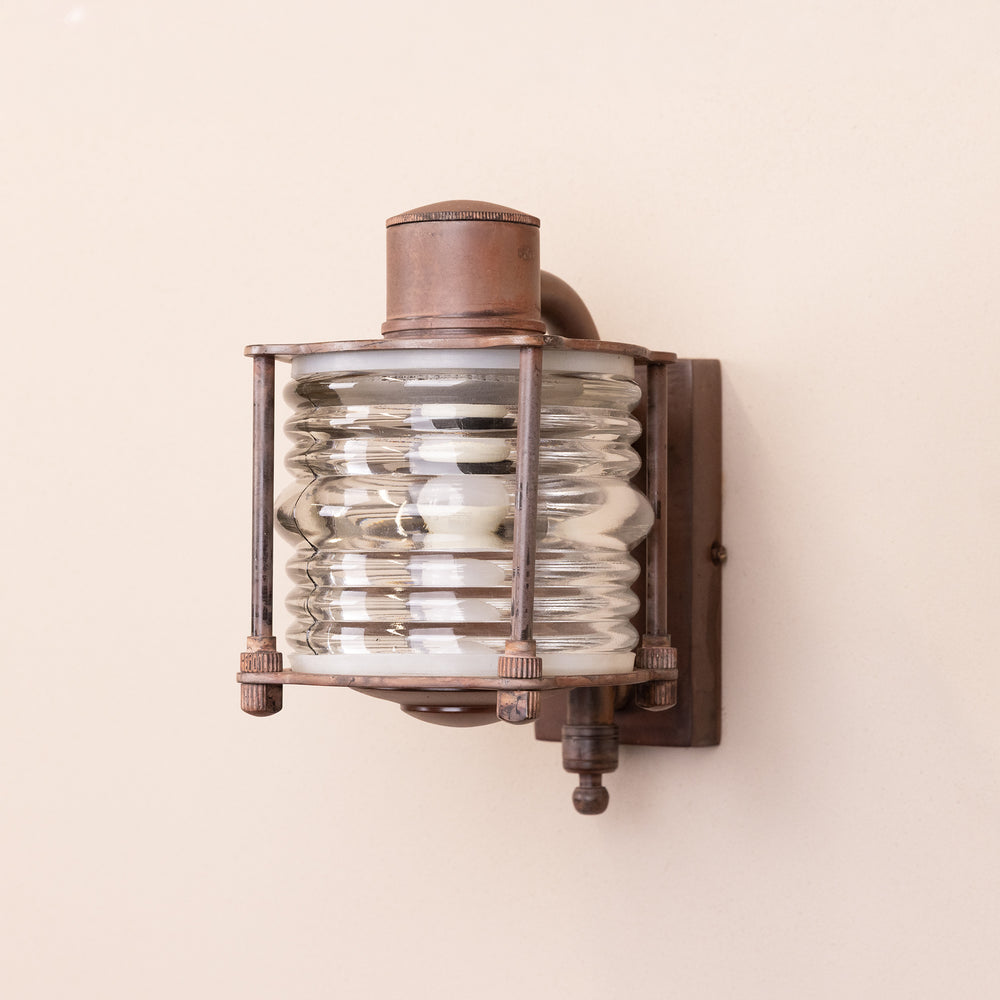 Angled image of the Agriframes Frome Outdoor Wall Lamp in a Rust finish with its bulb switched off, mounted on a neutral-coloured wall.