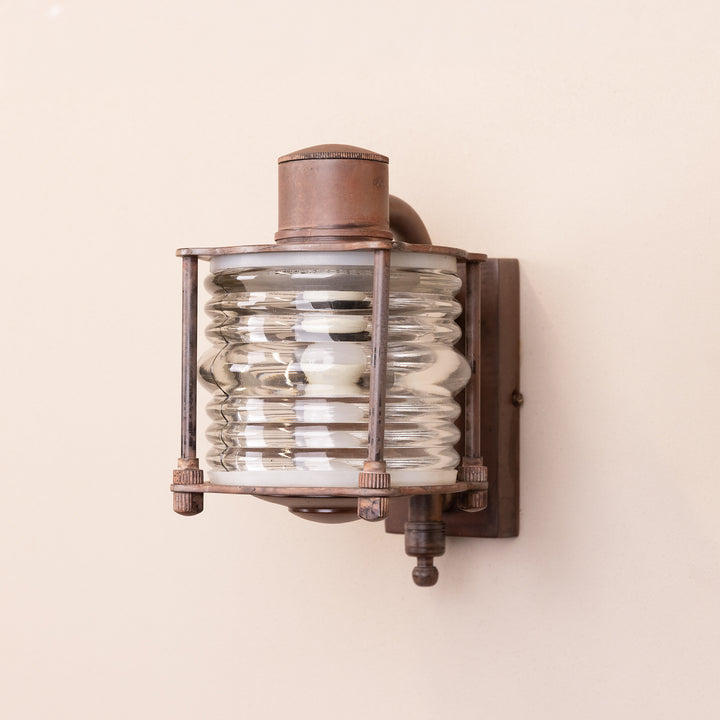 Angled image of the Agriframes Frome Outdoor Wall Lamp in a Rust finish with its bulb switched off, mounted on a neutral-coloured wall.