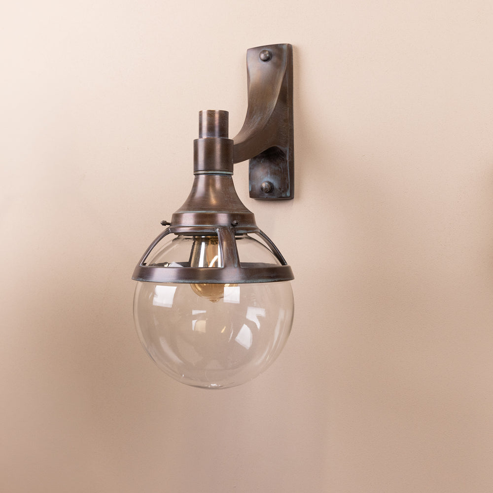 Angled image of the Agriframes London Outdoor Wall Lamp in a Copper Patina finish with its bulb turned off, mounted on a neutral background. 