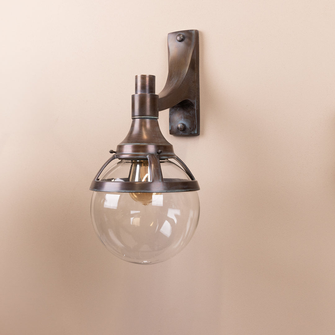 Angled image of the Agriframes London Outdoor Wall Lamp in a Copper Patina finish with its bulb turned off, mounted on a neutral background. 