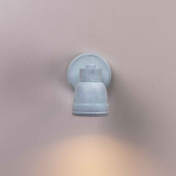 Agriframes Atworth Outdoor Lamp in an Aged Iron finish with its bulb illuminated mounted on an off white wall