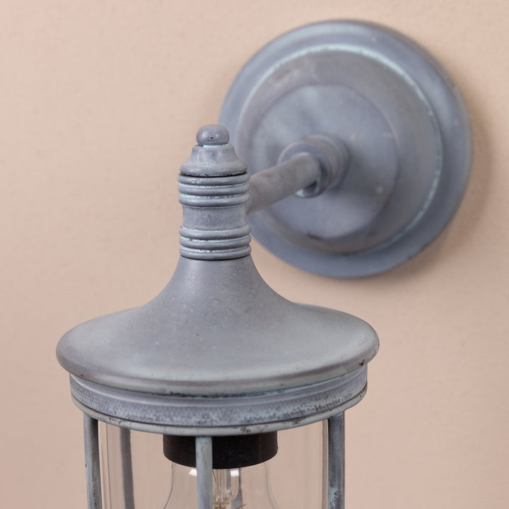 Closeup image of the base and stem of the Agriframes Chelsea Outdoor Wall Lamp in an Old Iron finish, mounted on a neutral background. 