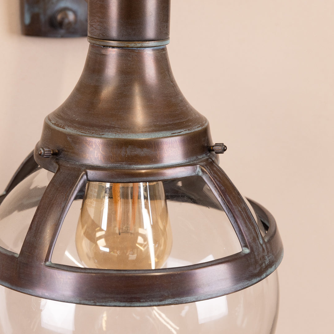 Closeup image of the Agriframes London Outdoor Wall Lamp in a Copper Patina finish, highlighting the bulb and glass casing area. 