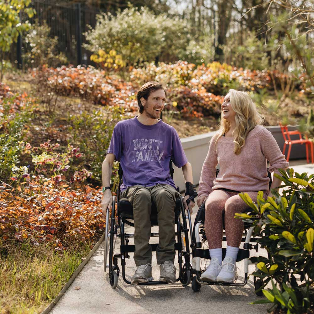 Two wheelchair-bound inviduals laughing together on a path in Horatio's Garden