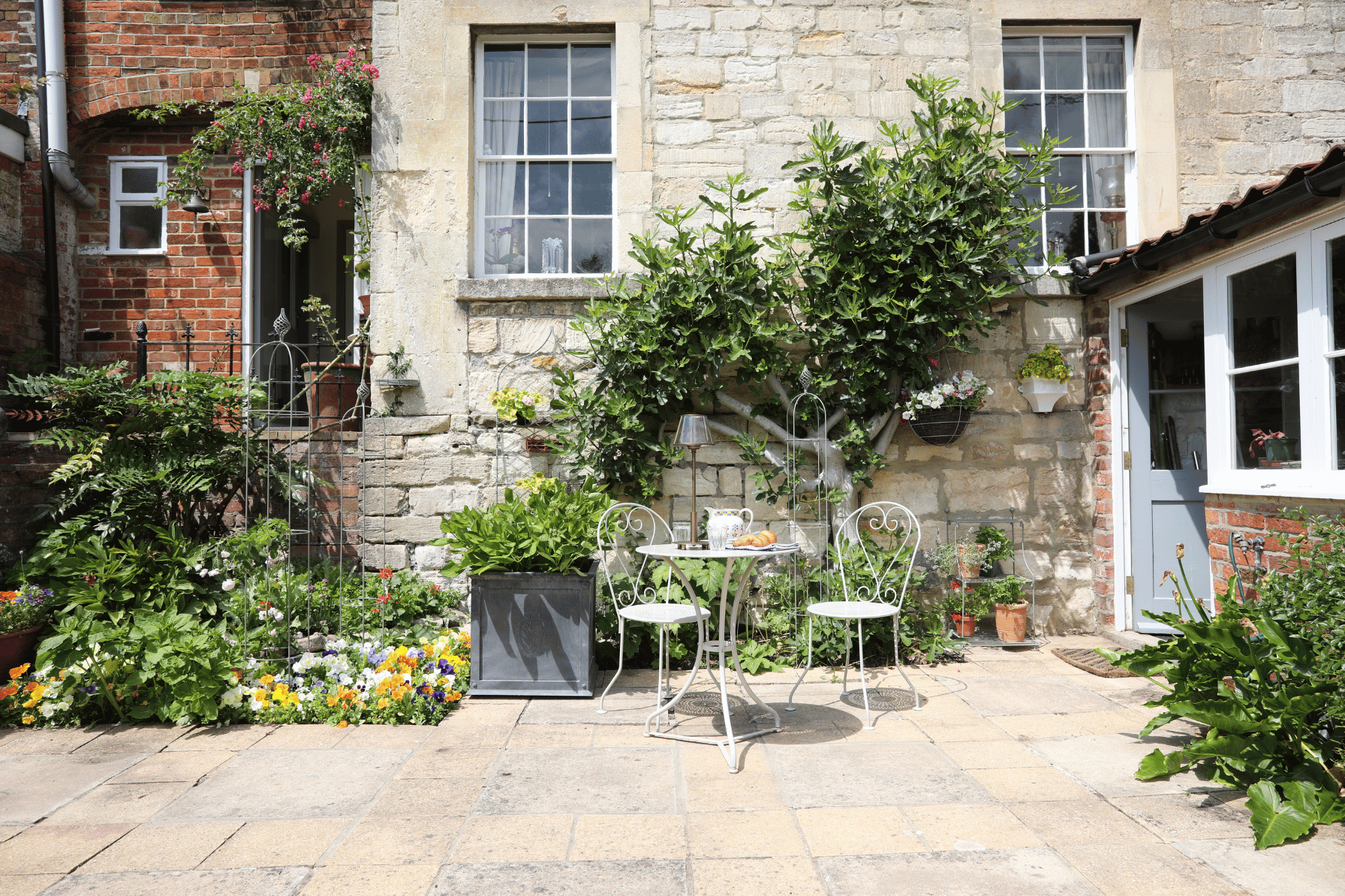 Small garden with a patio area, table, chairs, and stone building in the background.