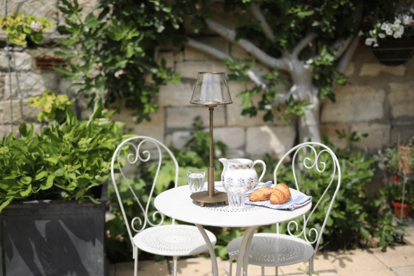 Outdoor setting with a small table and chairs, featuring a teapot and bread on a plate.