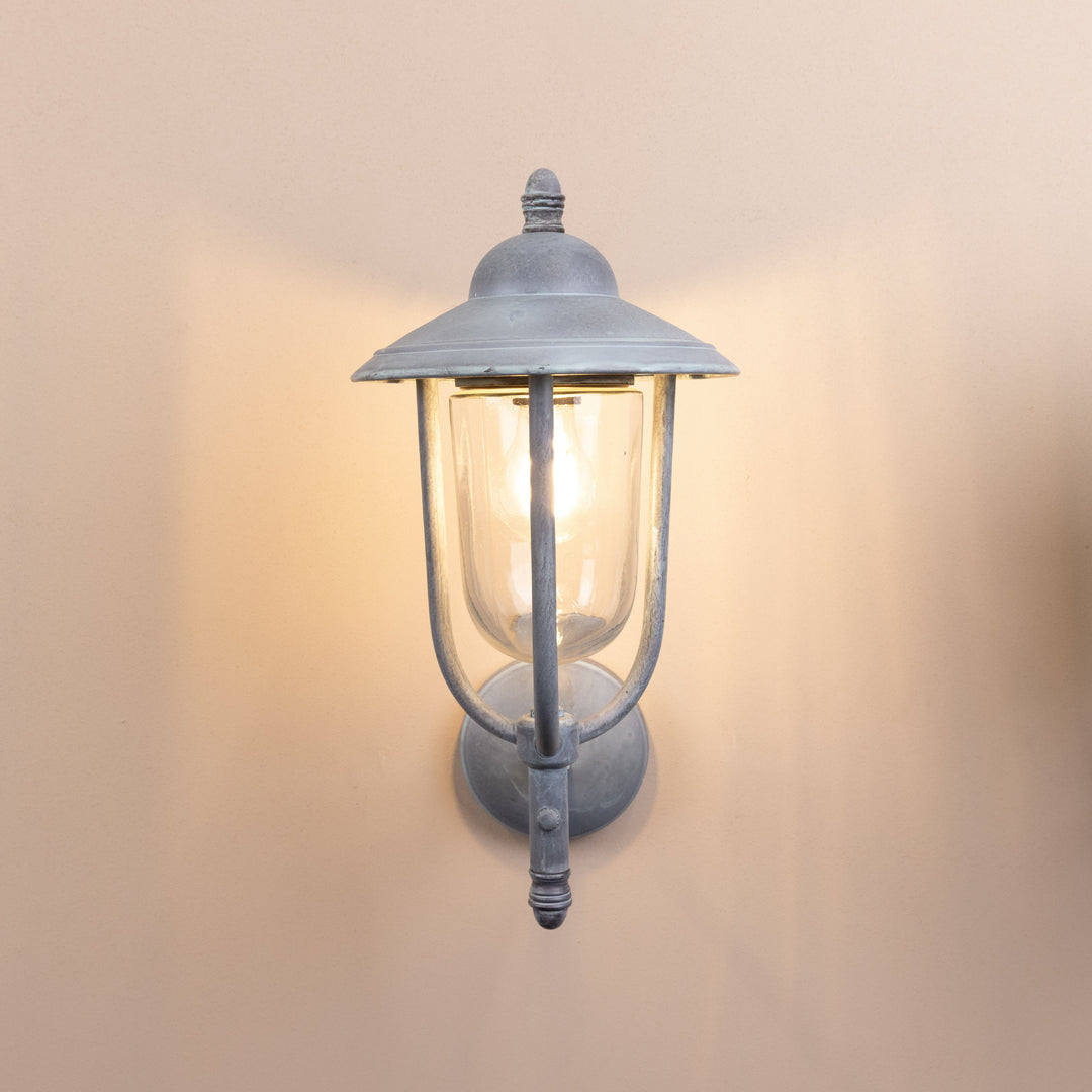 Front on image of the Agriframes Kensington Outdoor Wall Lamp in an Old Iron finish with its bulb switched on, mounted on a neutral background.