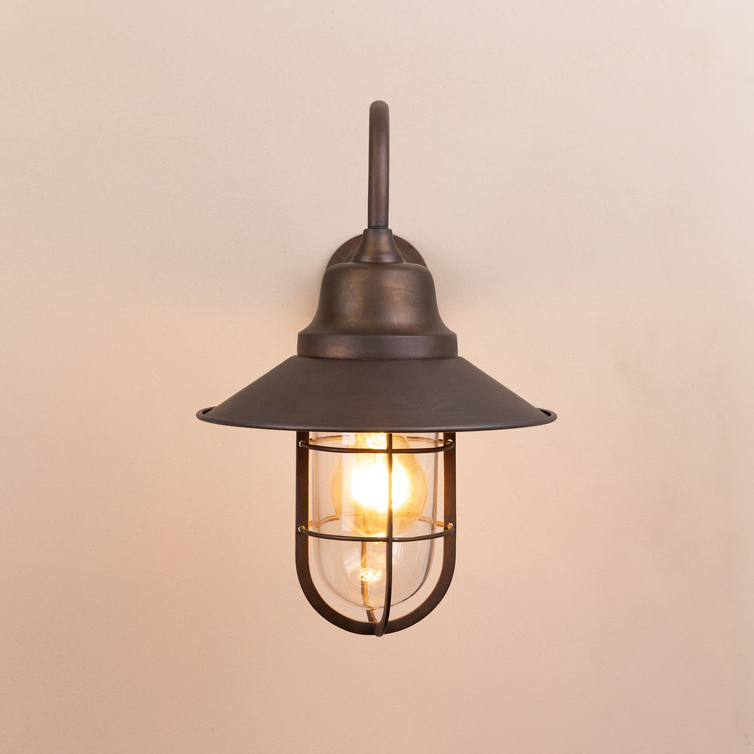 Front on image of the Agriframes Sidmouth Outdoor Wall Lamp in a Bronze finish with its bulb illuminated, mounted on a neutral background. 