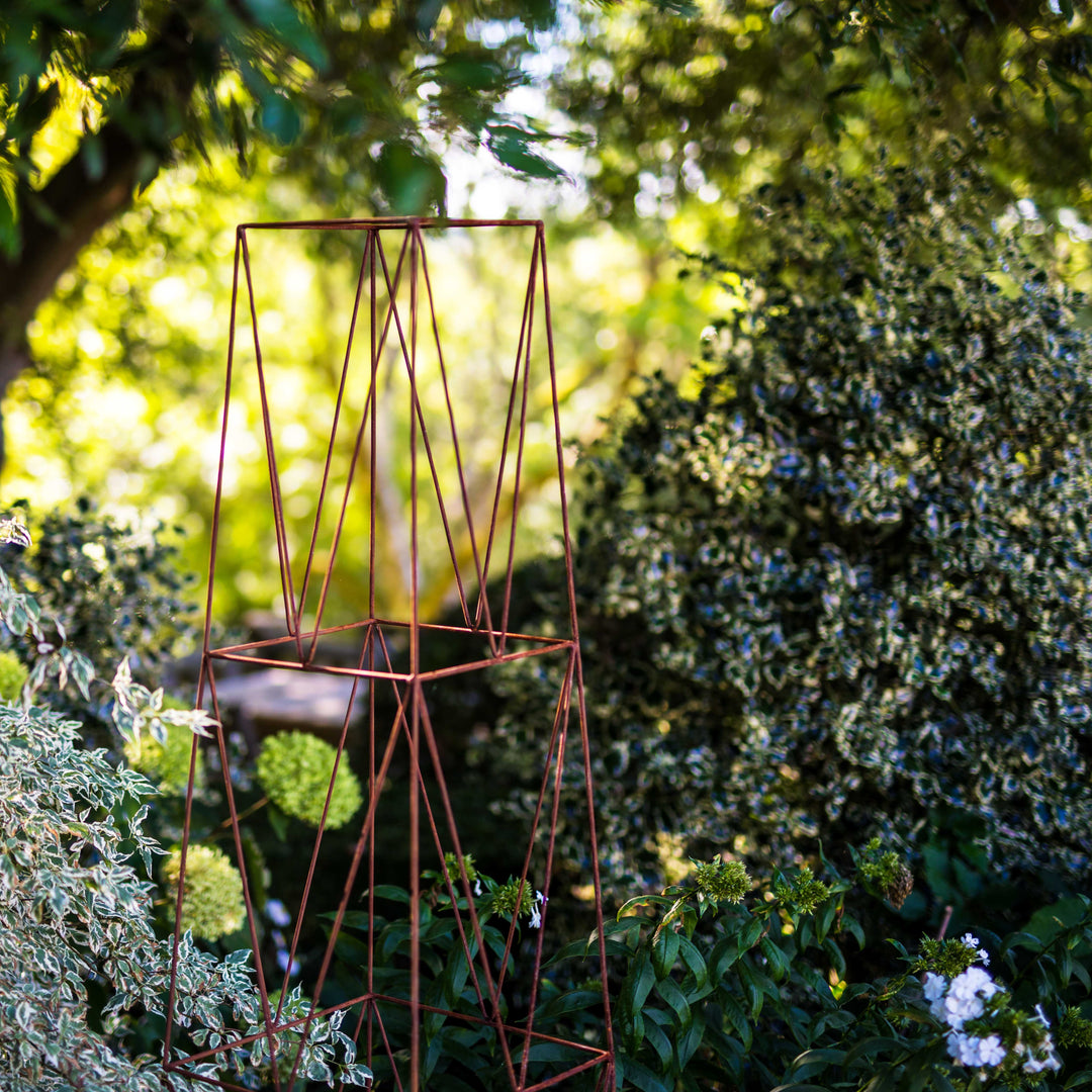 Top half of a Rustic Agriframes deco growing obelisk surrounded by shrubbery.
