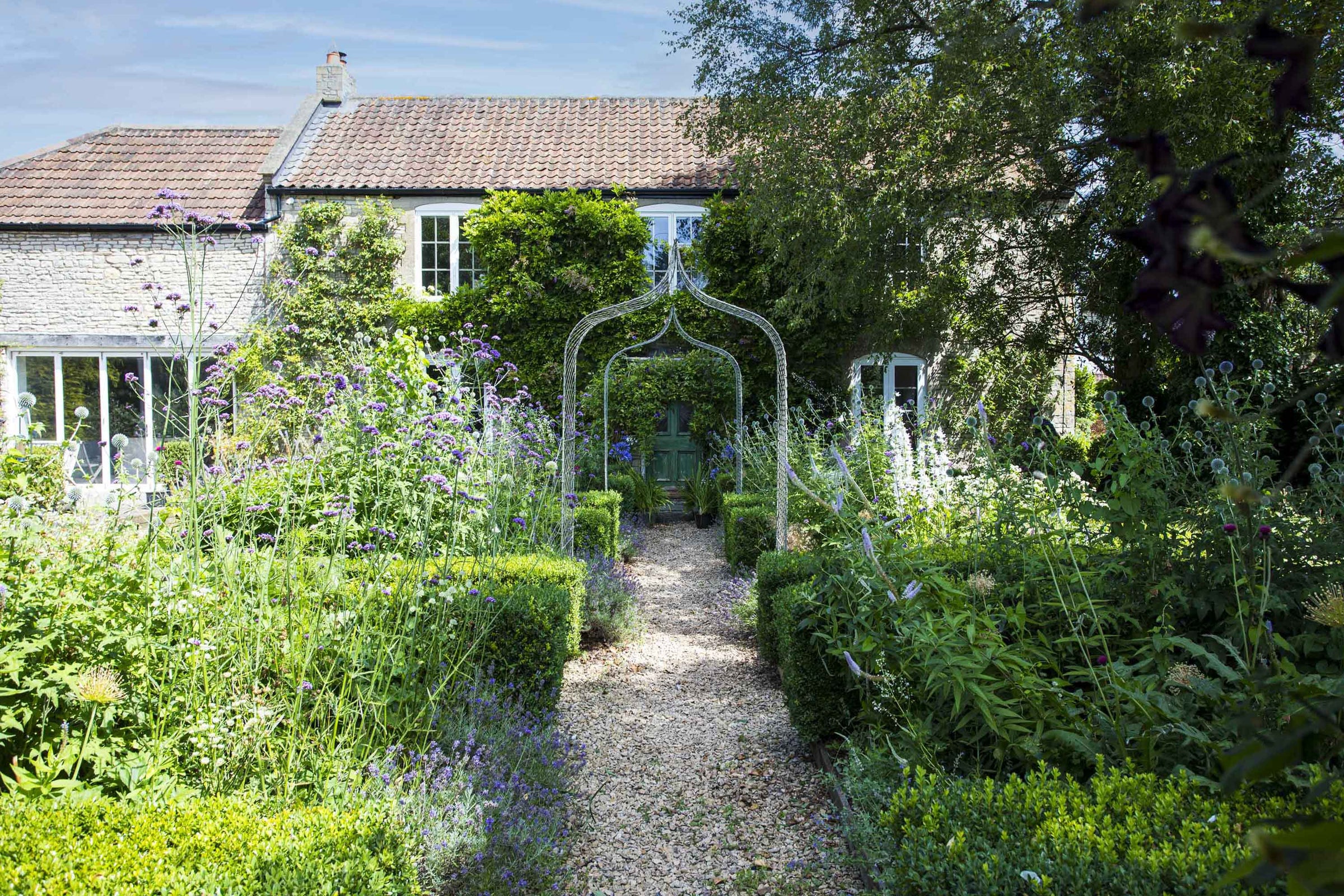 Agriframes elegance gothic arches over a garden path with flowerbeds either side and a cottage in the background