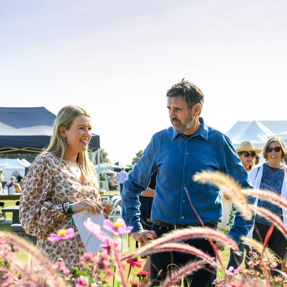 Two people walking through a flower garden with other people in the background