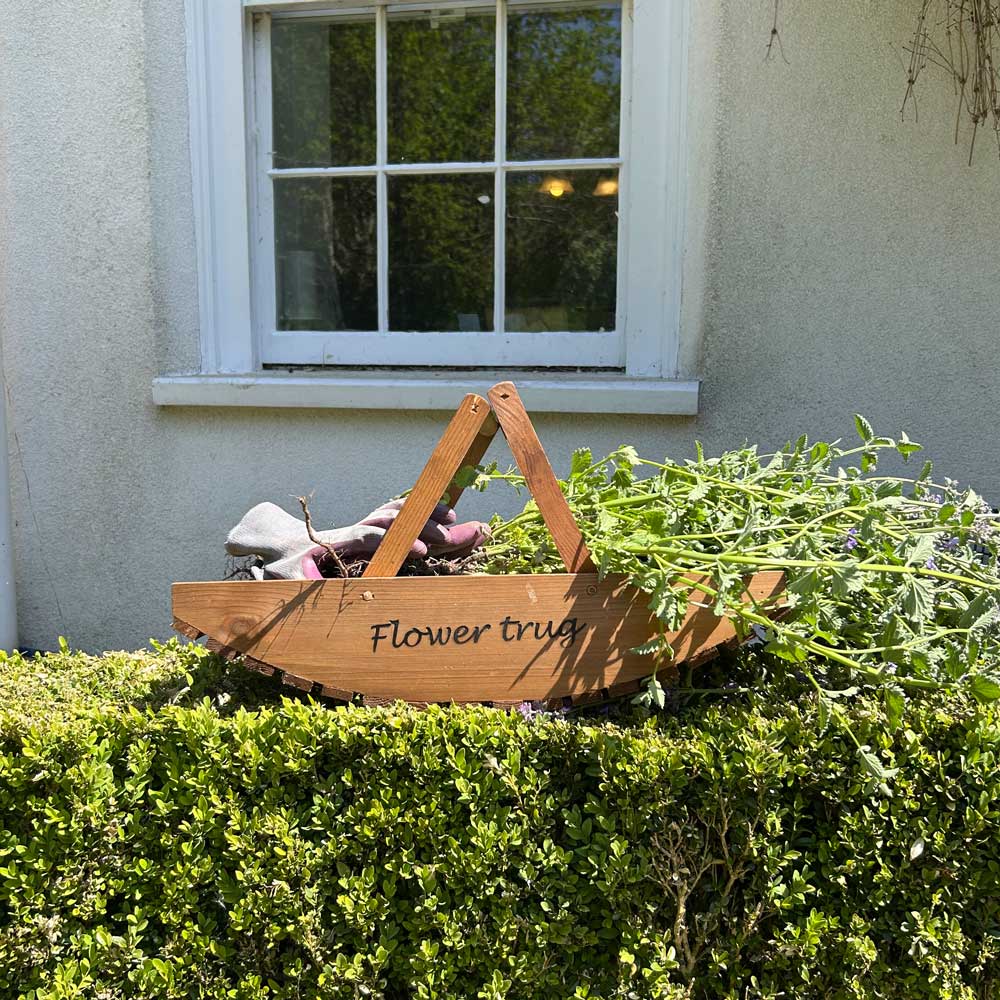 Wooden flower pot with 'Flower pot' label on a green bush in front of a window.