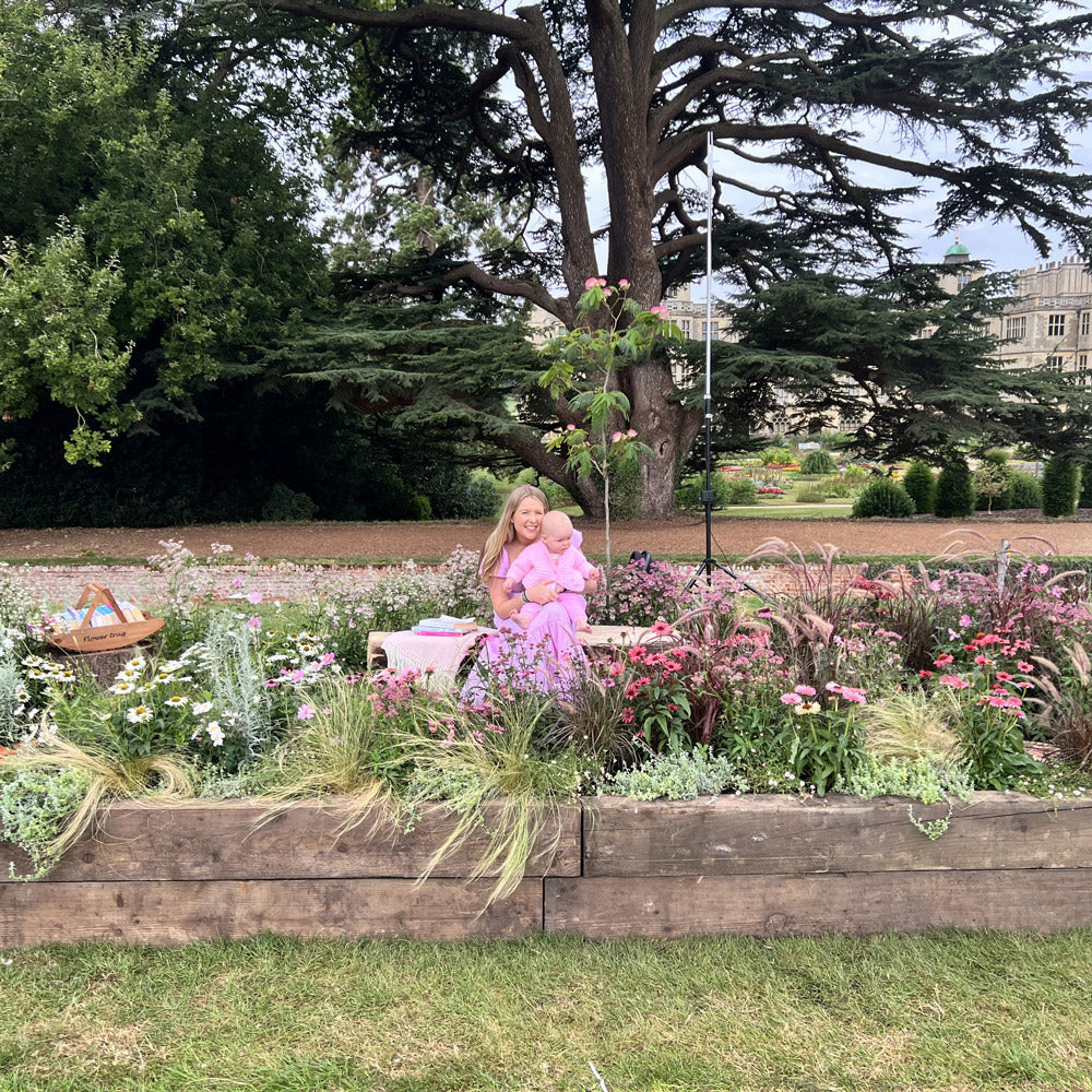 Woman holding a baby in a garden with flowers and trees